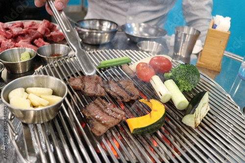 Korean Barbecue Grill Setup with Fresh Beef, Side Dishes, and Vegetables at Traditional Restaurant Table