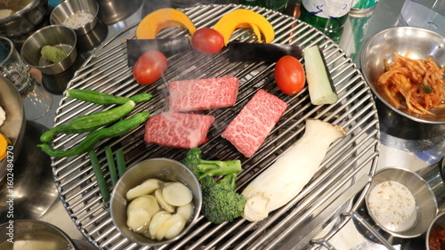 Korean Barbecue Grill Setup with Fresh Beef, Side Dishes, and Vegetables at Traditional Restaurant Table
