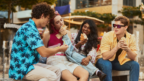 фотографія Group of young adults sitting on bench and eating street food together outdoors