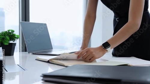 Woman wearing smart watch on wrist, flipping through meeting notebook, office desk in background