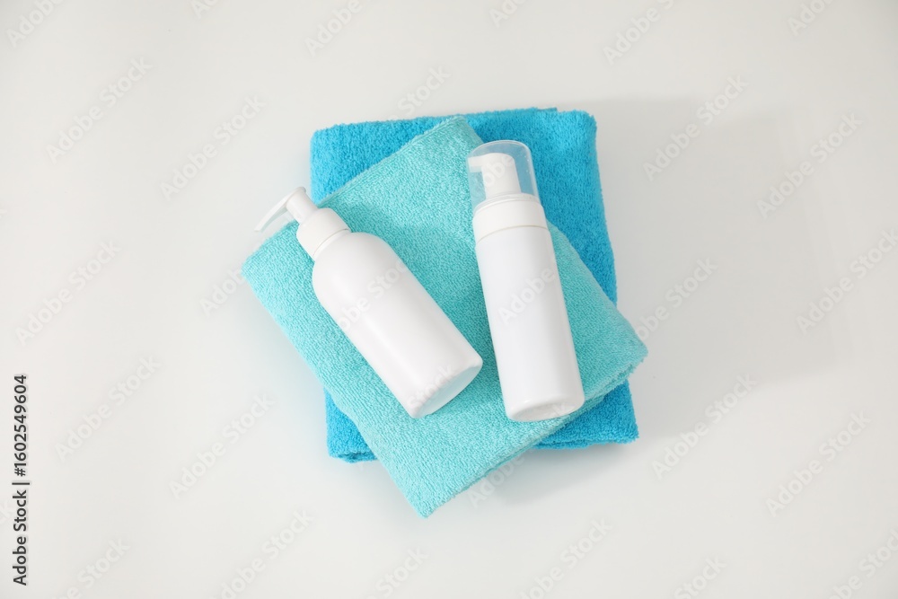 Fototapeta premium Stack of colorful towels and cosmetic products on white table, top view