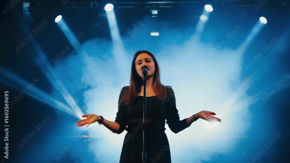 Silhouette of female singer standing under spotlight holding microphone on stage