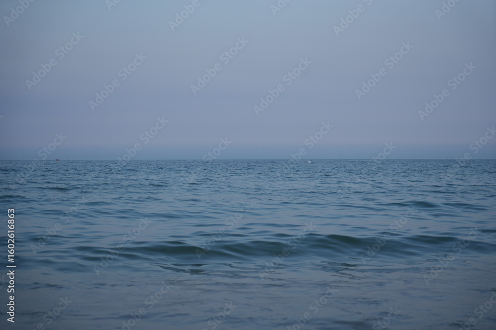 Fototapeta premium Calm sea at dawn with soft pastel blue and pink tones. Gentle waves approaching the shore under a peaceful, minimalistic horizon.