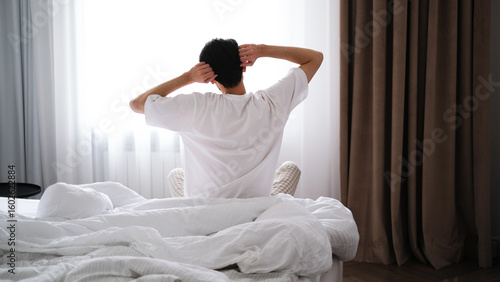 Wallpaper Mural Young brunet man stretching after sleep while sitting on a bed, back view Torontodigital.ca