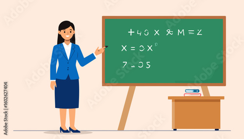 Smiling female teacher in a blue suit and skirt pointing at a green chalkboard with chalk.