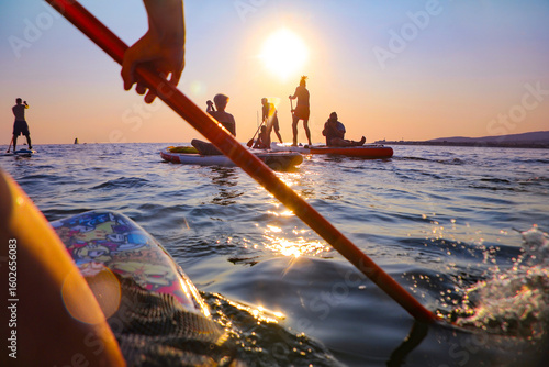 young people  riding  on sup surfing in the sea at sunset.