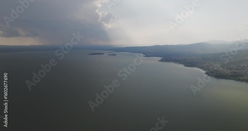 Wallpaper Mural Aerial view of the expansive Trasimeno Lake meeting the shore, with dark clouds contrasting the sunlit areas, Torricella, Umbria, Italy. Torontodigital.ca