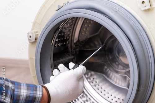 Washing machine repair: drum inspection. A hand with a screwdriver near the open washing machine drum, the process of appliance repair or maintenance