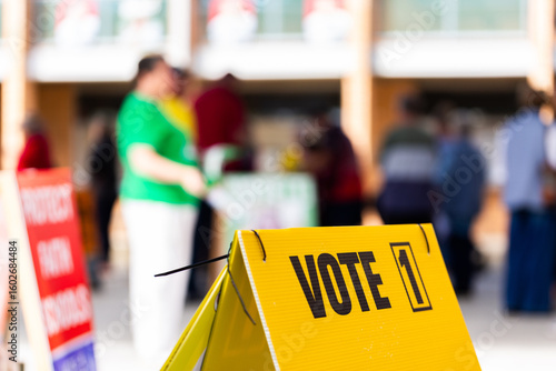 vote 1 on sign with out of focus voters waiting to enter polling station