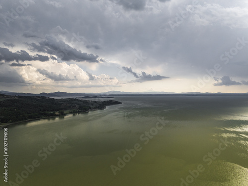 Aerial view of where the land kisses the tranquil lake under a sky heavy with brooding clouds near Trasimeno Lake, Torricella, Umbria, Italy.
