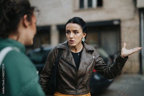 A woman wearing a leather jacket gesturing and showing frustration during a discussion with another individual. The background reveals an urban setting, enhancing the city-life narrative.