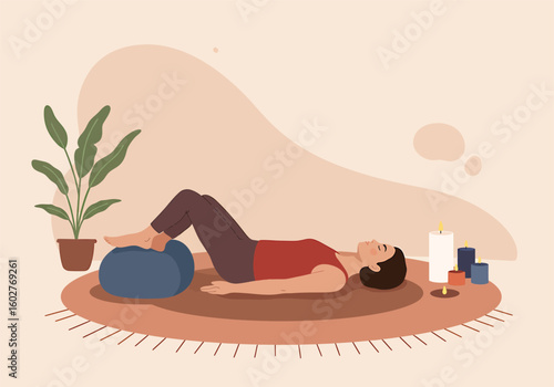 A person lying on a rug, resting with legs elevated on a blue pillow, surrounded by candles and a plant.