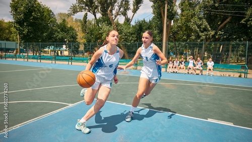 Bild auf Leinwand Two women engage in a game of basketball on an outdoor court beneath sunny skies