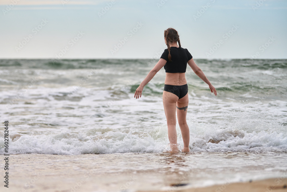 Young female, brown hair, stands calmly at baltic seas edge. Overcast sky, gentle waves create serene atmosphere. Focus on solitude and natural connection Young female, brown hair, stands calmly at baltic seas edge. Overcast sky, gentle waves create serene atmosphere. Focus on solitude and natural connection