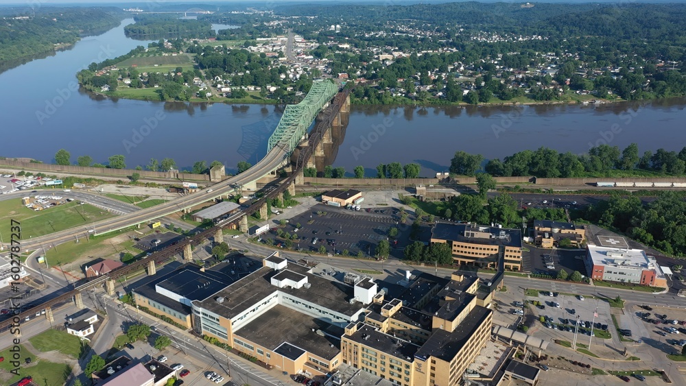 Fototapeta premium Panoramic aerial view of Parkersburg, West Virginia, featuring the Ohio River, Little Kanawha, and downtown buildings amidst lush Appalachian landscape.
