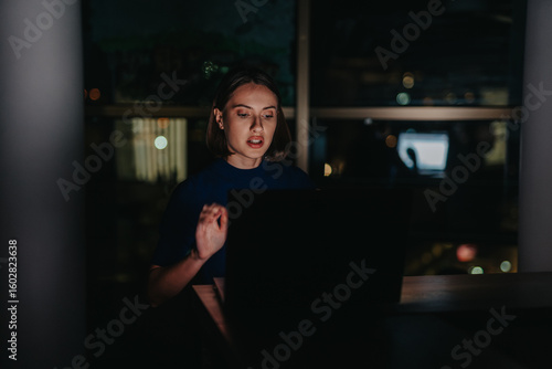 Fotografie A dedicated businesswoman works intently on her laptop at night, focusing in a dimly lit office setting