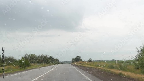 view from inside car window on rain water drops falling on glass with blurred trees nature background at summer spring day.