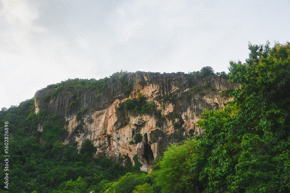 Naklejka premium A view of large limestone mountains covered with dense green forest. Limestone mountains are characterized by steep cliffs, natural cracks and fissures that reveal different layers of rock.