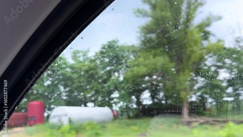 view from inside car window on rain water drops falling on glass with blurred trees nature background at summer spring day.