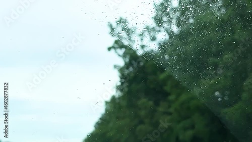 view from inside car window on rain water drops falling on glass with blurred trees nature background at summer spring day.