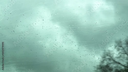 Car view on road with green trees and cloudy sky in rainy weather. Raindrop on glass.