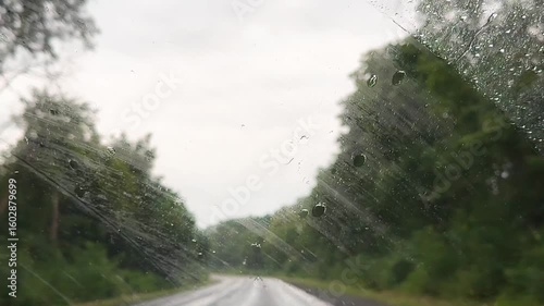 view from inside car window on rain water drops falling on glass with blurred trees nature background at summer spring day.