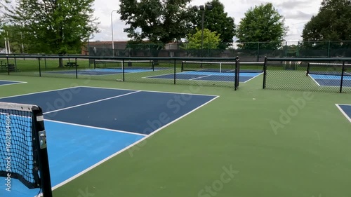 Outdoor Pickleball Courts. Sweeping views in motion of empty pickleball courts. Moving forward across several courts in a row. Public city park setting with cloudy blue Summer sky.