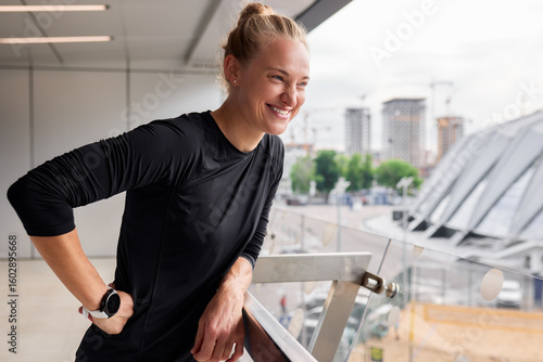 Fit woman smiling by a balcony with city view and casual posture Free Download Fit woman smiling by a balcony with city view and casual posture - GFXLoad