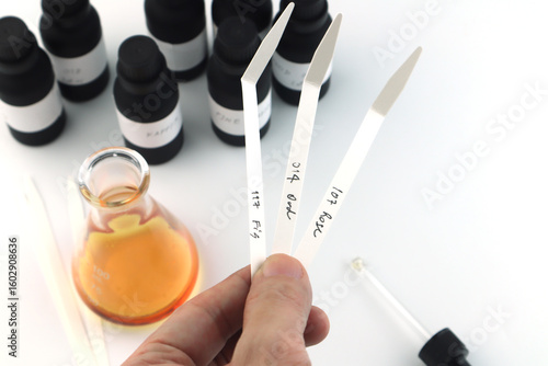 blotter papers in left hand is used in scent testing, essential oil ,fragrance oil bottle for testing smell during blending process for choosing nice scent for scented candles and body perfume in lab