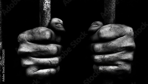Two hands clasped tightly on metal bars against a black background