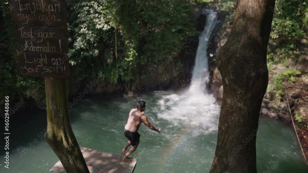 Man jumps off a platform into the turquoise plunge pool of Kroya Waterfall, Bali a thrilling tropical adventure in the heart of the jungle. Man jumps off a platform into the turquoise plunge pool of Kroya Waterfall, Bali a thrilling tropical adventure in the heart of the jungle.