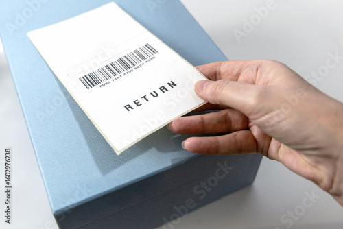 A woman's hand holds a return label over the blue box