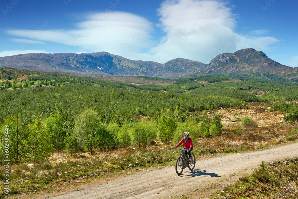 Fototapeta premium nice senior woman riding her electric mountain bike in the highlands of Glen Affric Nature reserve, Scotland, UK