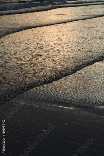 A serene beach at sunset, with soft waves reflecting the golden light and creating gentle patterns on the sand.