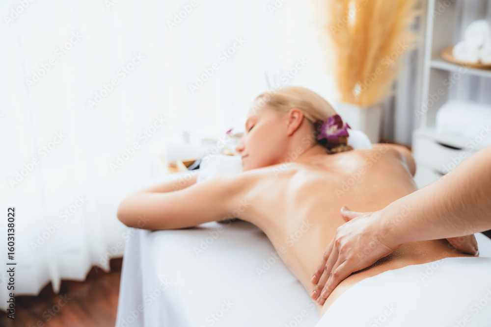 Naklejka premium Caucasian woman customer enjoying relaxing anti-stress spa massage and pampering with beauty skin recreation leisure in day light ambient salon spa at luxury resort or hotel. Quiescent