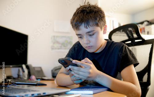 Teenage boy using smartphone in study room at home,Preteen child holding mobile cell phone apps playing games,checking social media,Child addiction to internet,gadget,cyber bullying and safety concept