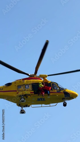 Positano,Italy-20 07 2025:Italian yellow rescue helicopter lifting rescuer and injured person on steel cable from seaside accident on the Amalfi Coast. Intense emergency action in dramatic coast