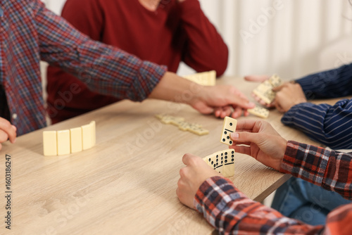 Friends playing dominoes at light wooden table indoors, closeup