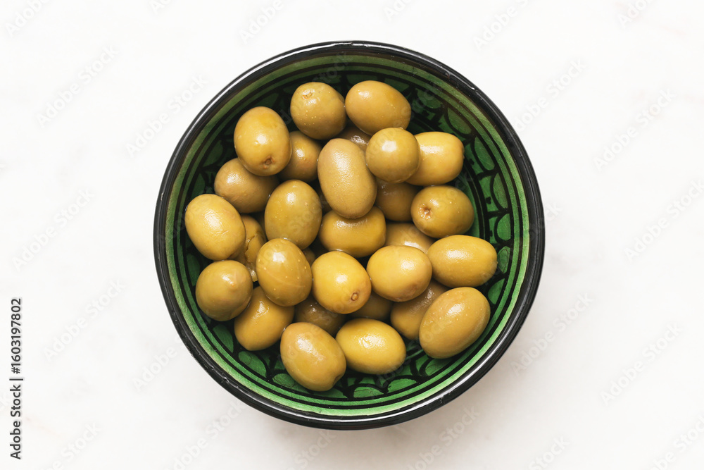 Green olives in ceramic bowl. Top view of traditional Moroccan dish. White marble background with copy space. Healthy Mediterranean snack. Natural food rich in flavor and nutrition. Flat lay style. Green olives in ceramic bowl. Top view of traditional Moroccan dish. White marble background with copy space. Healthy Mediterranean snack. Natural food rich in flavor and nutrition. Flat lay style.