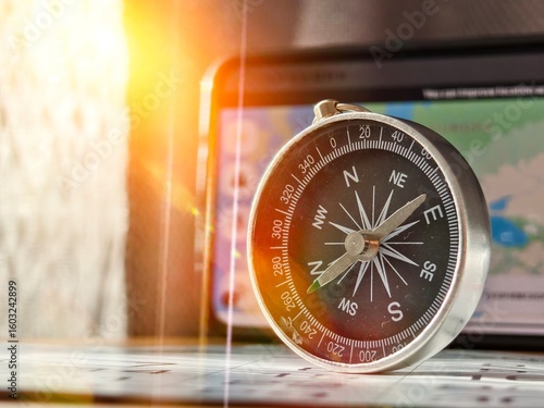 A close-up shot of a person holding a vintage-style compass with a metallic finish and clear markings for cardinal directions (N, S, E, W) and degree measurements. The compass is being used in conjunc