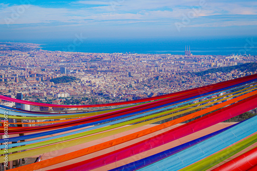 Photography Panoramic view of Barcelona and the Mediterranean Sea with colorful ribbons in the foreground, creating a vibrant contrast between urban architecture and festive decoration