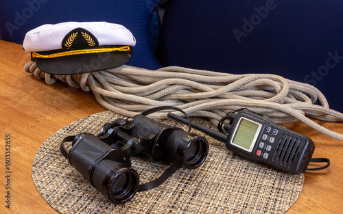 Marine binoculars and a handheld VHF marine radio and captain's hat with a rope on a boat table
