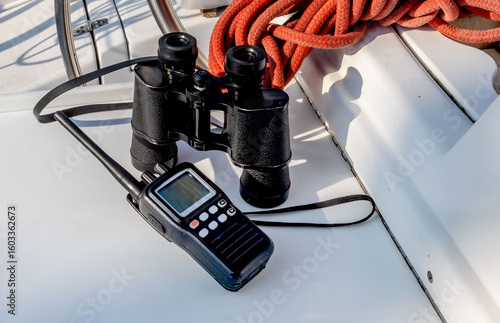 A handheld VHF marine radio and binoculars on a sailboat table