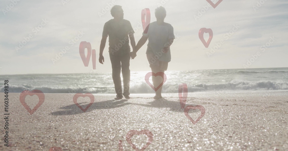 Obraz premium Holding hands senior couple walking along sunlit shoreline, with red heart and location-pin icons
