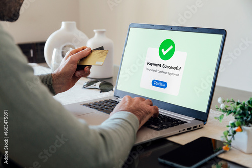 Making a credit or debit card payment online. Successful digital payment confirmation on a laptop screen. Man in his living room completing a purchase.