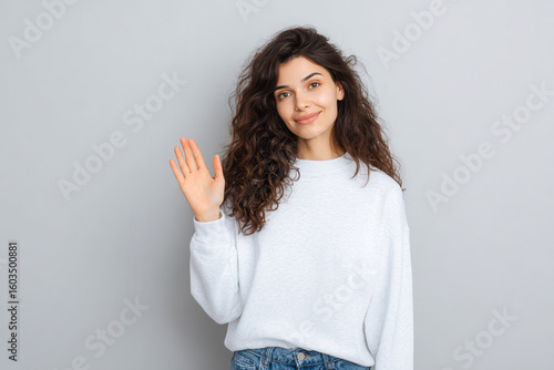 cheerful individual is playfully waving hello with open palm against clean neutral background