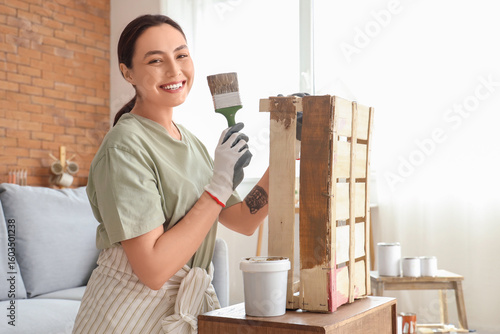 Foto Young woman with brush painting wooden box at home