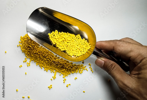 Yellow plastic masterbatch, polymer carries colorful pigments with small scoops poured into a white background, suitable for product catalog design of industrial plastic manufacturing company profiles