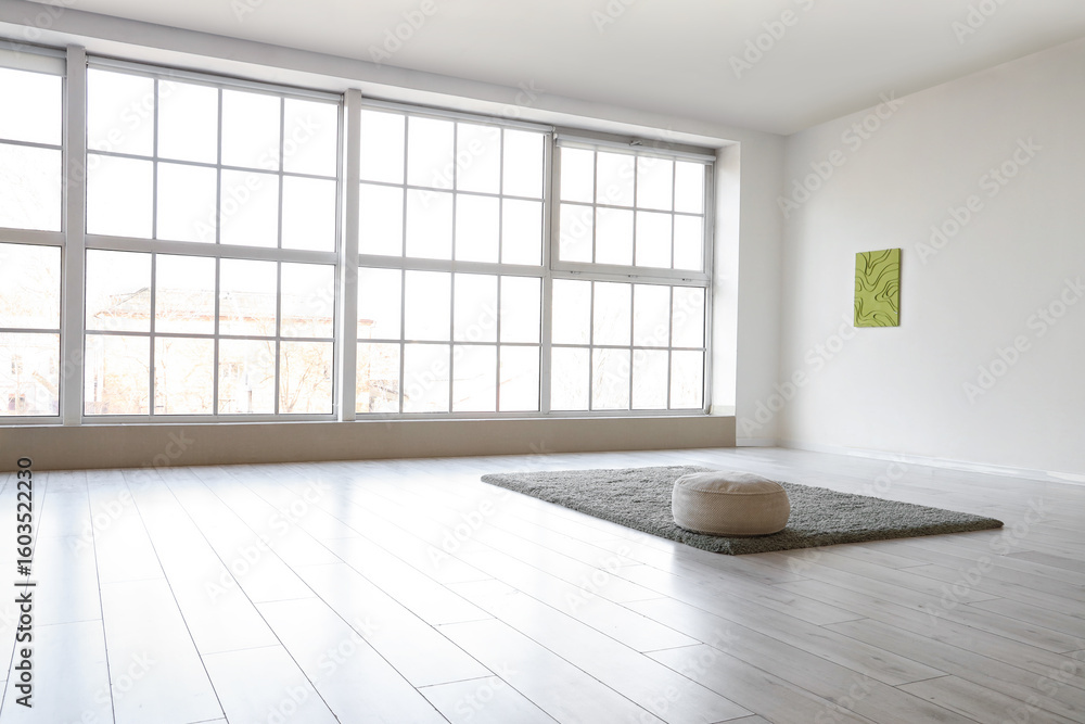Obraz premium Pouf with carpet and painting on light wall in big room