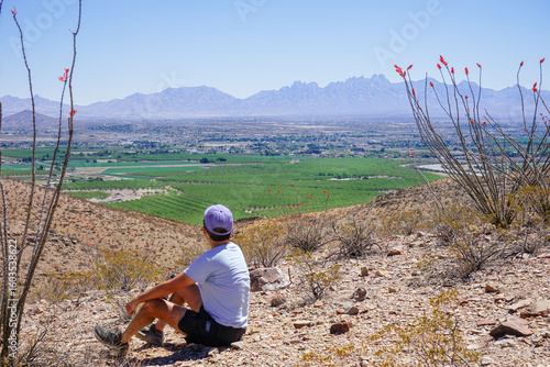 Lone hiker sits on a hiking trail in the Prehistoric Trackways National Monument on the Robledo Mountains overlooking agricultural fields in Las Cruces, New Mexico and the Organ Mountains